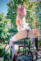 A woman with pink hair sitting on a stool.