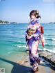 A woman in a kimono standing on a beach next to the ocean.