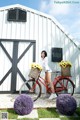 A woman standing next to a red bike with a basket full of flowers.