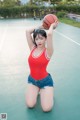 A woman in a red shirt and denim shorts holding a basketball.