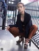 A woman sitting on a bench wearing a black blazer and brown pants.