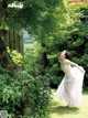 A woman in a white dress standing under a tree.